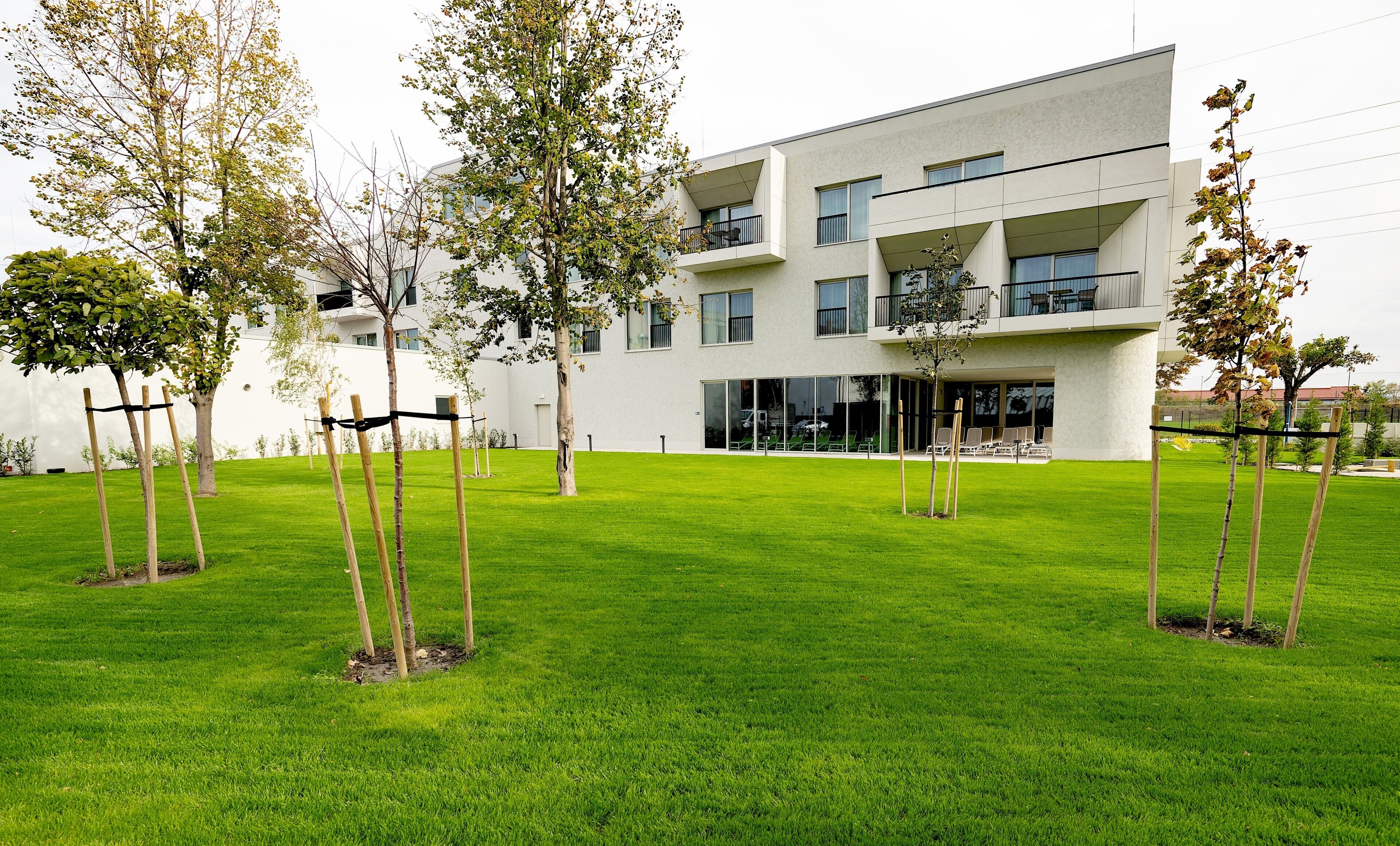 A modern building with a flat roof, multiple balconies, and a well-maintained lawn with young trees.