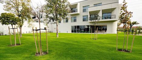 A modern building with a flat roof, multiple balconies, and a well-maintained lawn with young trees.