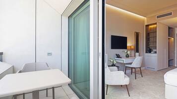 Una habitación de hotel moderna con puerta corredera de vidrio, un área de comedor con mesa y sillas, un televisor de pantalla plana montado en la pared y una estantería empotrada.