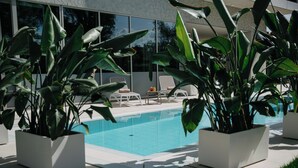 Un área de piscina moderna al aire libre con dos sillas reclinables blancas y plantas en macetas.