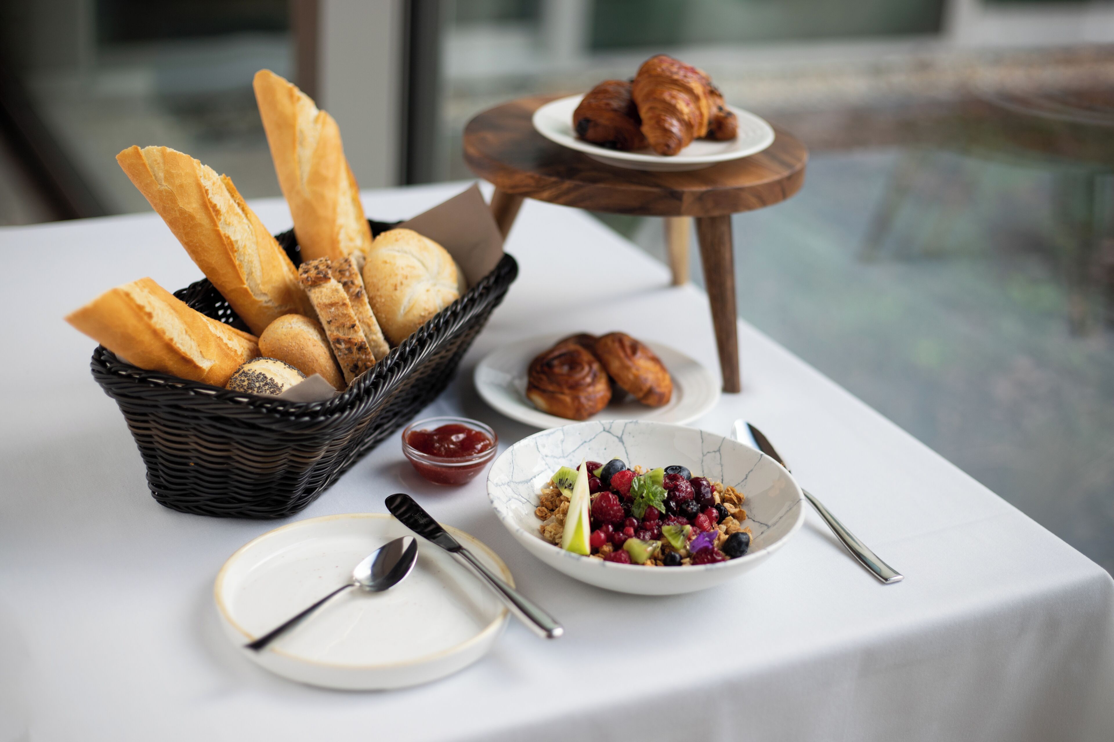 A breakfast setting with bread, pastries, and a bowl of fruit salad on a table.
