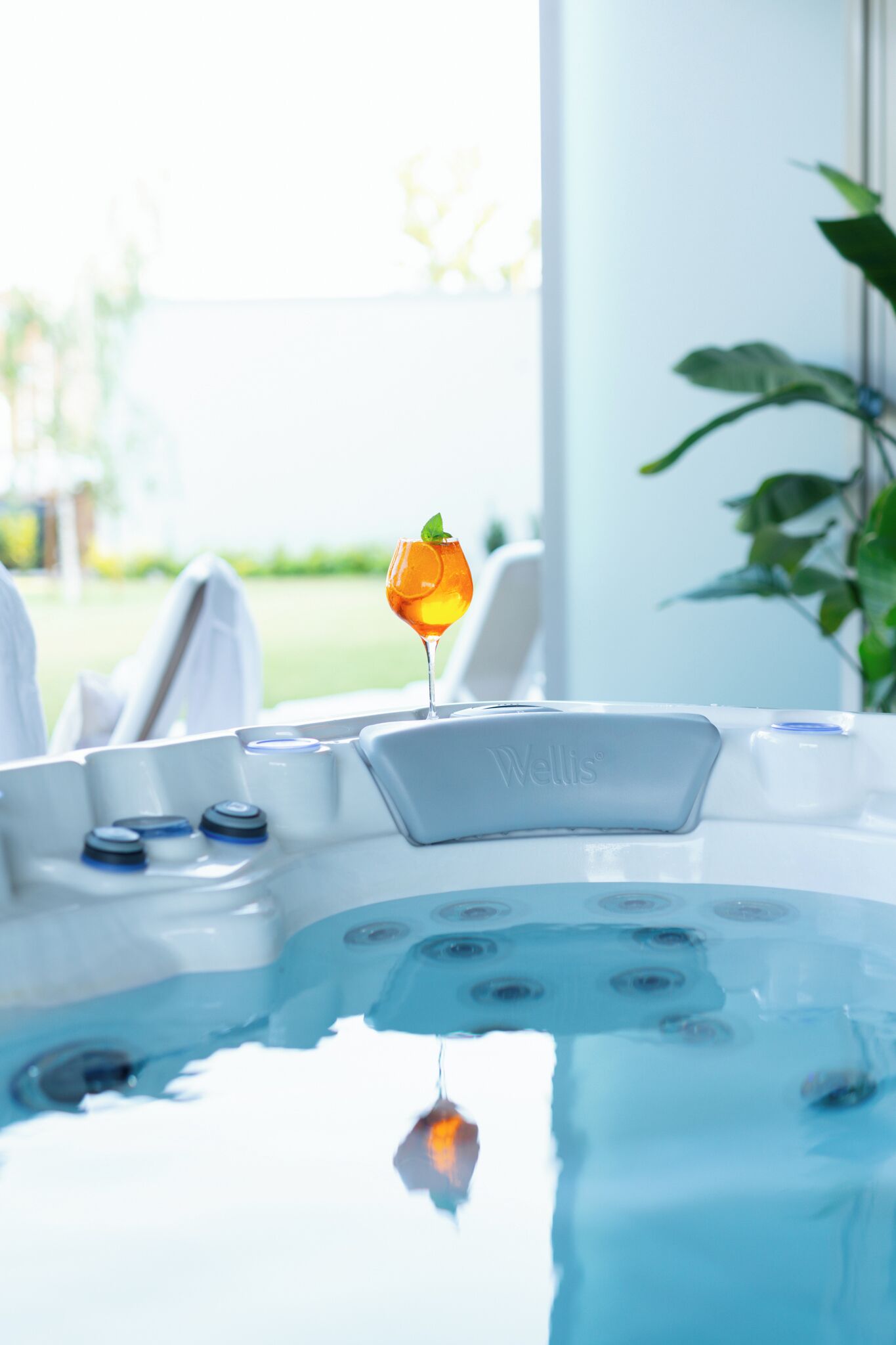 A hot tub with a glass of orange juice and a mint leaf, surrounded by white towels and a Wells brand water heater.