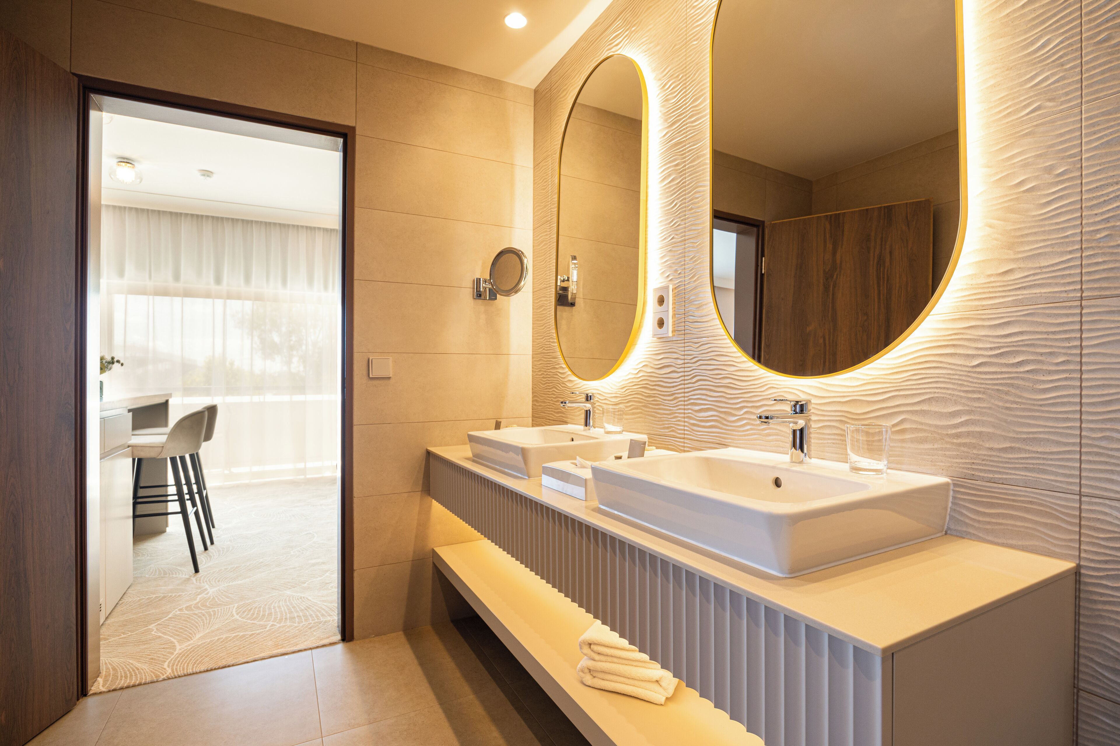 Une salle de bain moderne avec deux lavabos, un grand miroir et un meuble-lavabo doté d’un porte-serviettes.