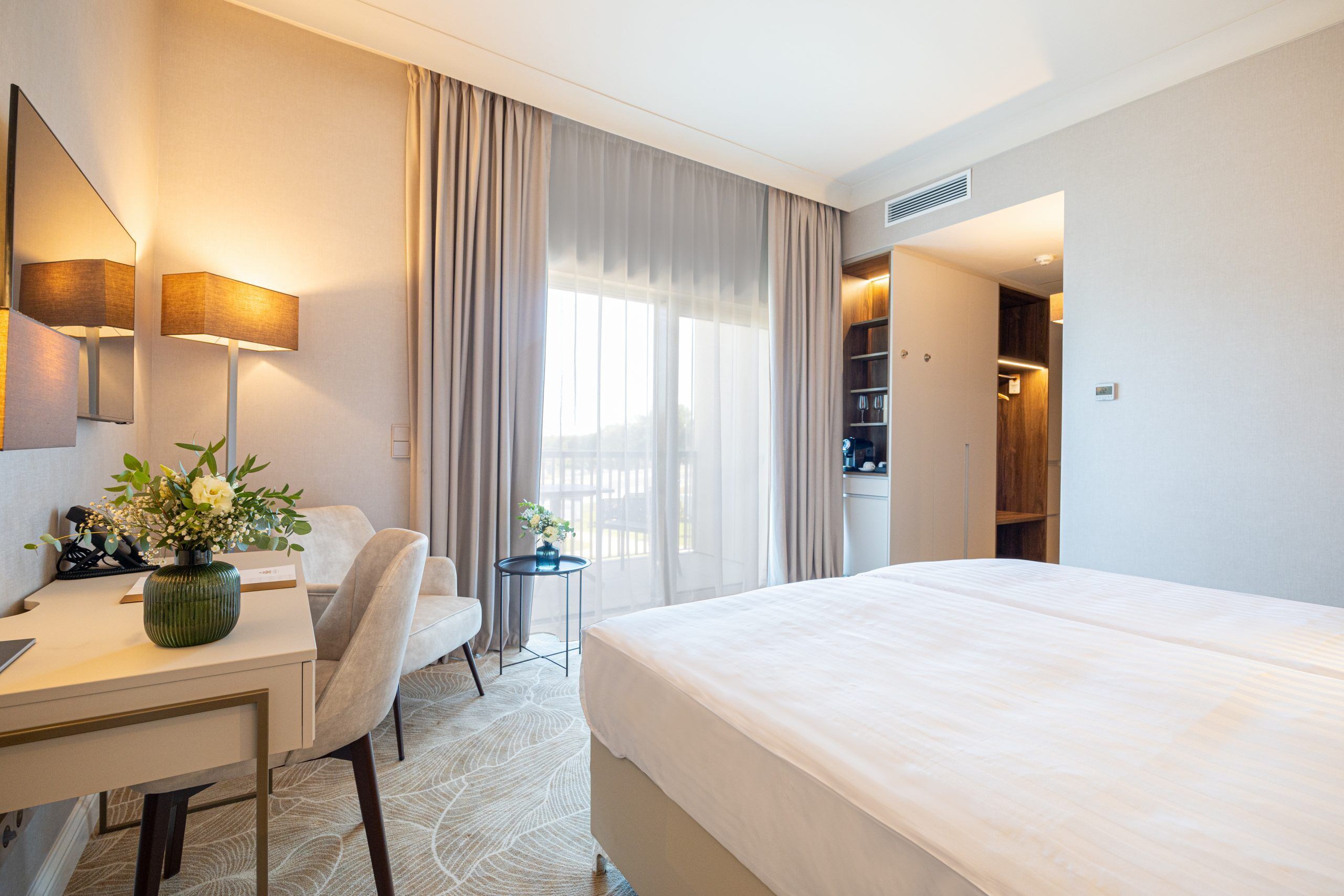 Una habitación de hotel con cama, escritorio, silla y una mesita con un florero.