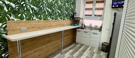 A modern kitchen with a wooden counter, a window with striped curtains, and a built-in air conditioner.