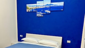 A hotel room with a large bed, a blue wall, and a cityscape artwork. - punto house ferrovia (Naples)