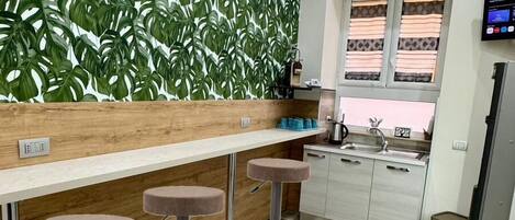 Una cocina moderna con encimera de madera, tres taburetes de bar, aire acondicionado integrado y una ventana con persianas.