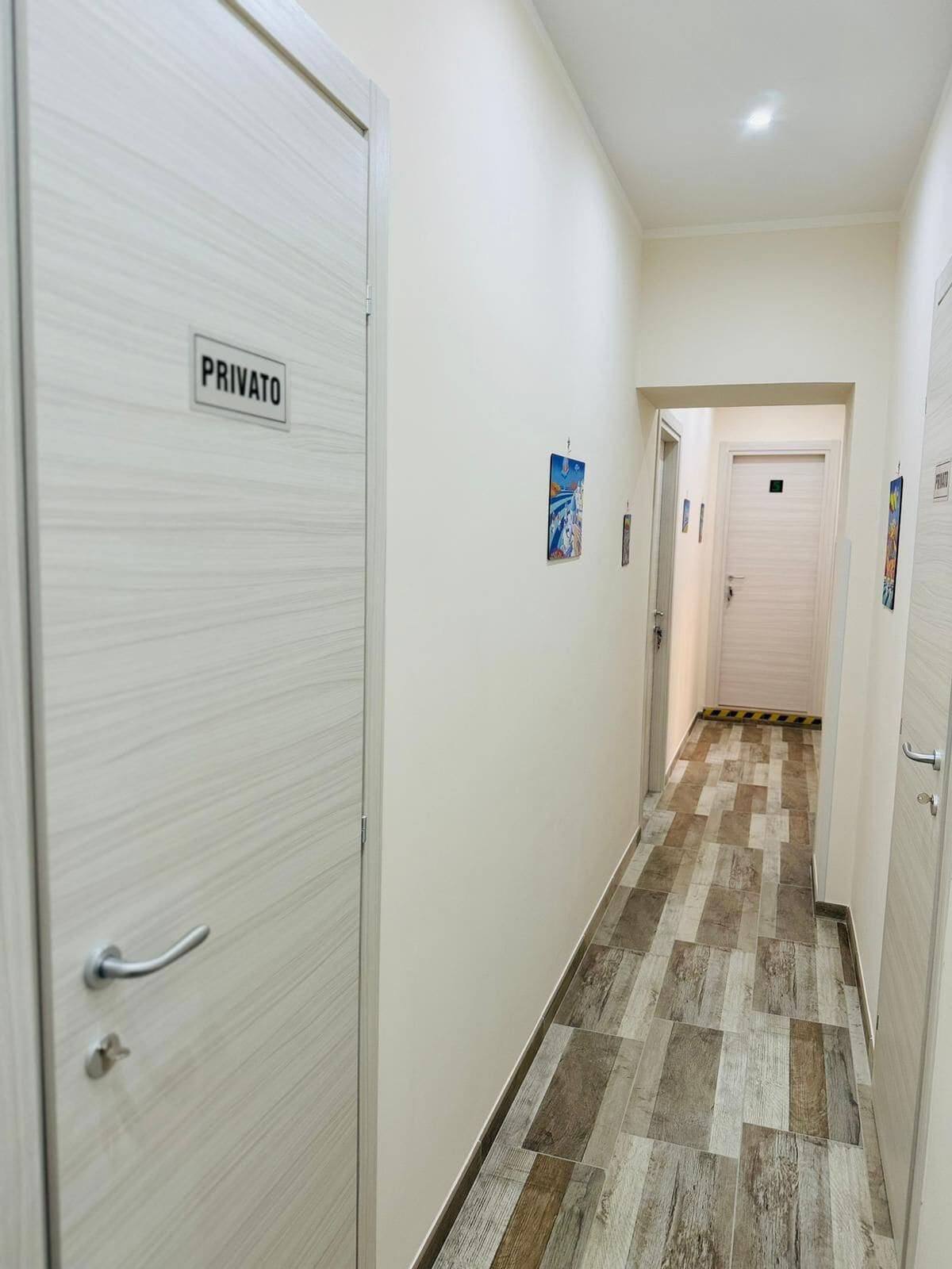 A hallway with a 'PRIVATO' sign on a door, patterned flooring, and a door at the end.