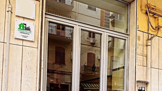 A building with a large glass door, a sign for "Punto House Ferrovia", and a visible manhole cover on the ground. - punto house ferrovia (Naples)