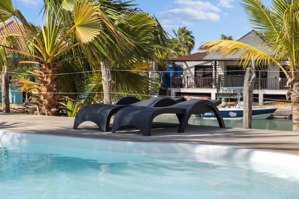A pool area with lounge chairs, palm trees, and a boat docked in the background. - Caribbean Lofts 61 - Waterfront (Kralendijk)