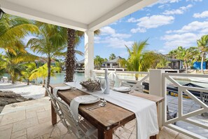 A dining area with a table set for two, overlooking a pool and palm trees. - Caribbean Lofts 61 - Waterfront (Kralendijk)