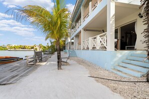 A beachfront property with a wooden dock, a palm tree, and a building with a blue exterior and white balcony railings. - Caribbean Lofts 61 - Waterfront (Kralendijk)
