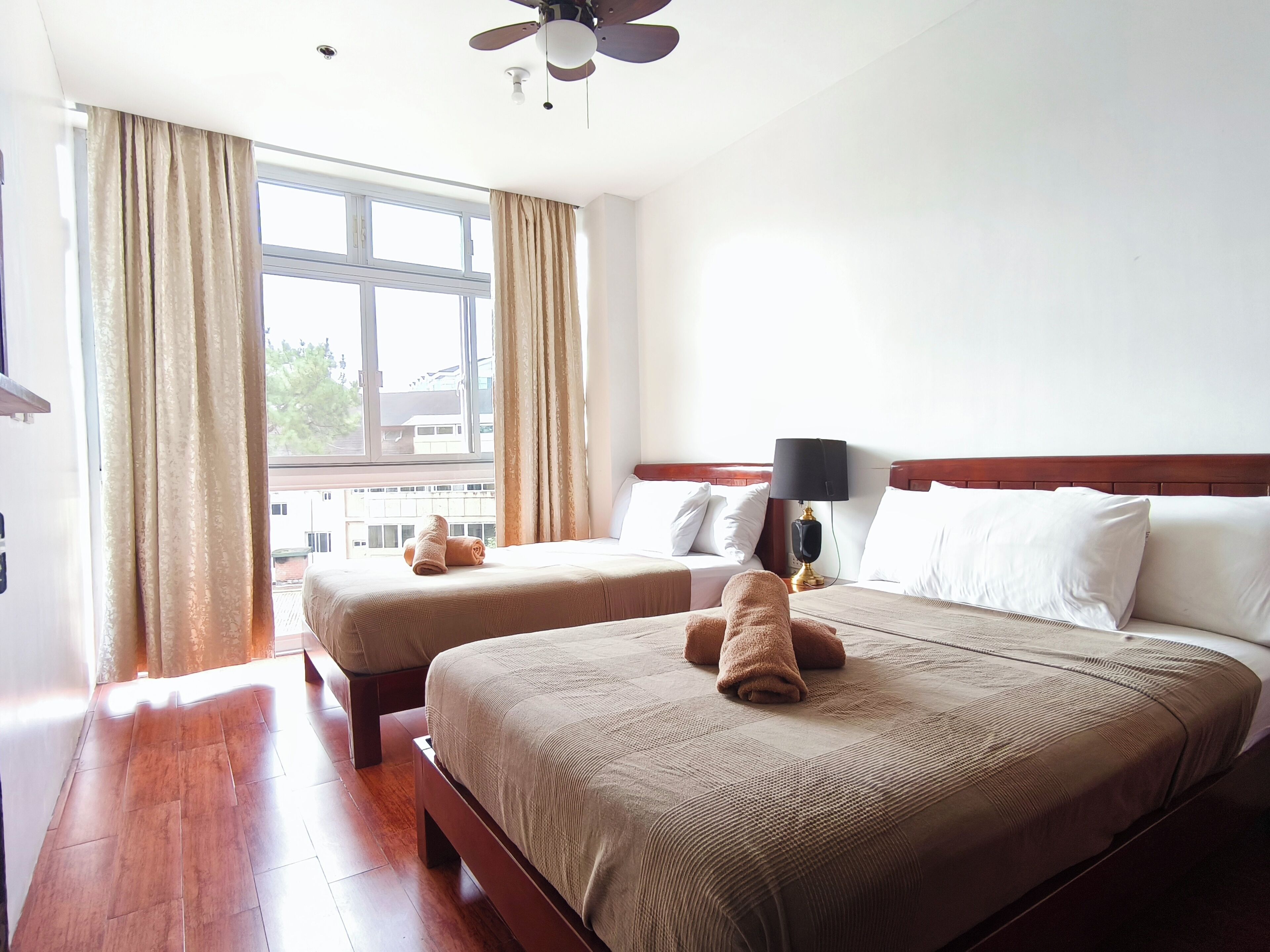 A hotel room with two beds, a ceiling fan, and a window with curtains.