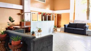 A spacious lobby with a grey sofa, a coffee table, and potted plants. There is a reception desk with a white counter and a decorative garland. - Grandview Residences by Vilma near Burnham Park-204 (Baguio)