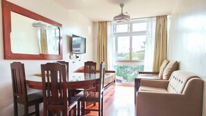 A room with a dining table, chairs, a sofa, a TV, and a window with curtains. - Grandview Residences by Vilma near Burnham Park-204 (Baguio)