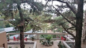 A balcony with potted plants and red chairs, overlooking a courtyard with trees and a building in the background. - Grandview Residences by Vilma near Burnham Park-204 (Baguio)