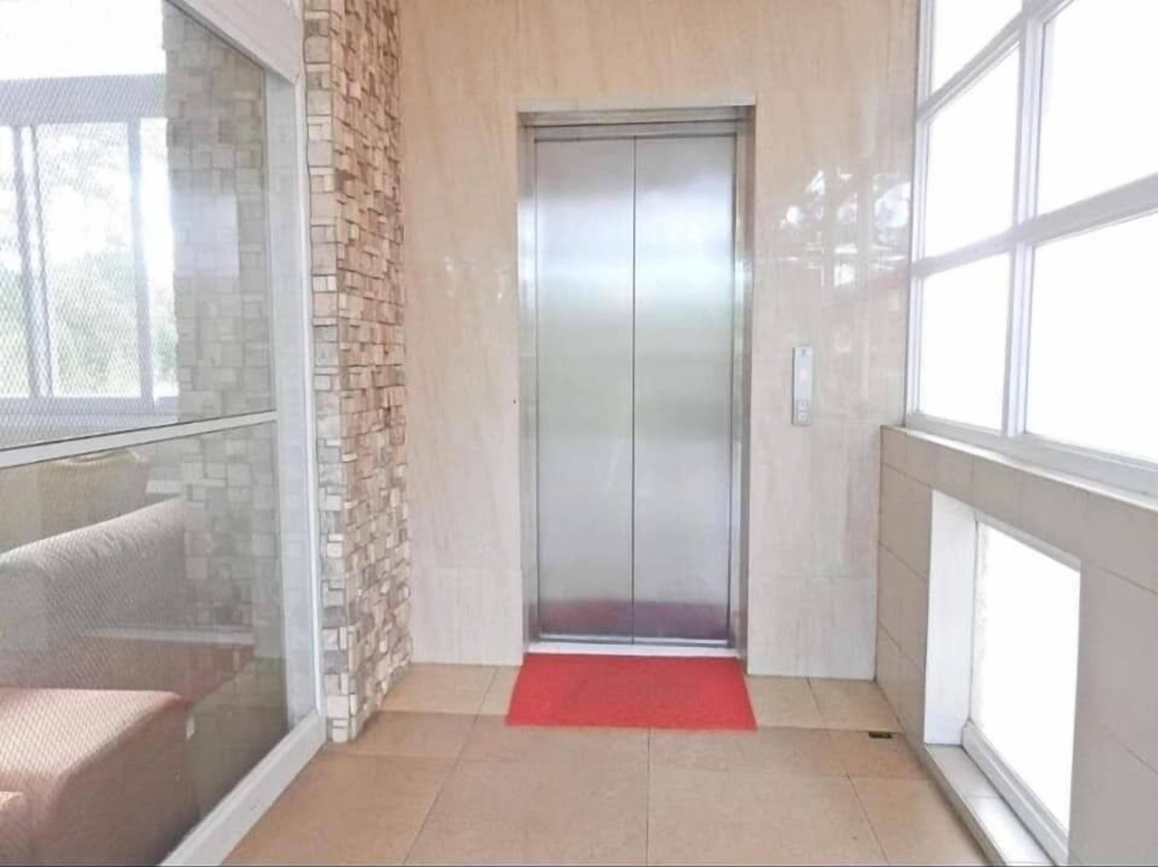 An elevator in a hallway with a red carpet, a glass wall, and a tiled floor.