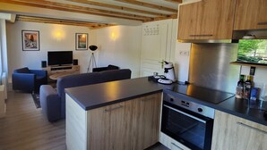 Cozinha compacta com forno embutido, sala de jantar com mesa e cadeiras, e área de estar com sofá e televisão.