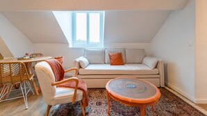 Un acogedor apartamento tipo loft con techo alto, un ventanal grande, un sofá, una silla, una mesita y un tapiz estampado.