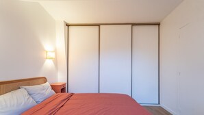 Un dormitorio con cama, mesita de noche, lámpara de pared y armario de puertas correderas.