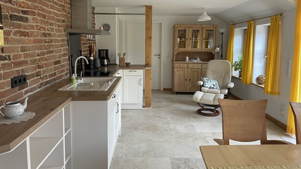 Una cocina pequeña con pared de ladrillo, armarios blancos y una mesa de comedor de madera.