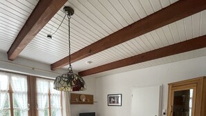 Una sala de estar acogedora con techo de madera, un sofá con cojines blancos, una mesita de madera y un televisor sobre un mueble de madera.