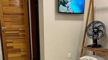 Une chambre à coucher avec un lit, un téléviseur fixé au mur et un ventilateur sur pied.