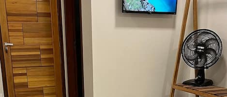 Un dormitorio con cama, televisor montado en la pared y ventilador de pie.