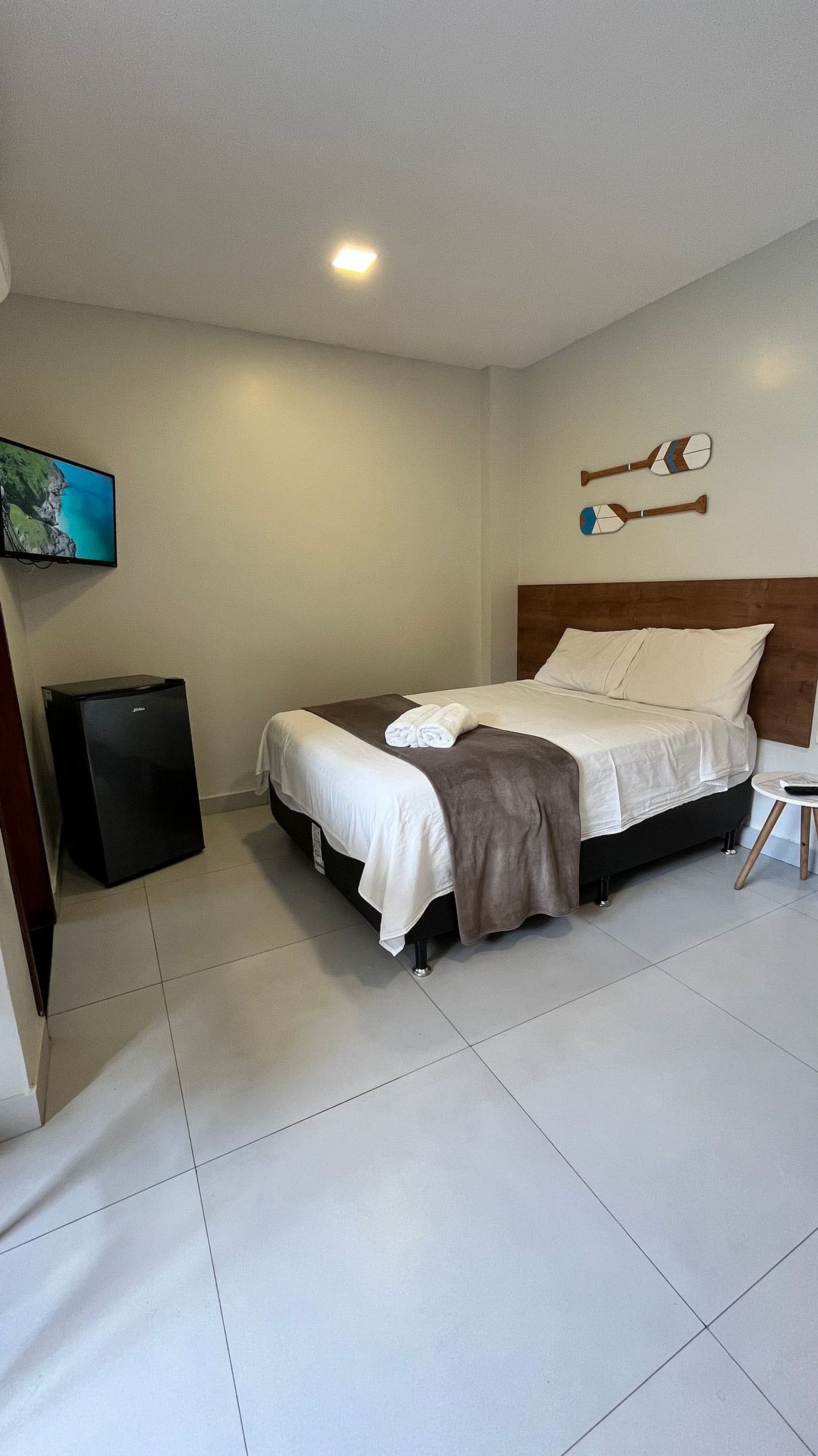 Habitación de hotel con cama, televisor, refrigerador pequeño y un perchero en la pared.