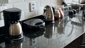 A kitchen with a microwave, coffee maker, kettle, and dish rack. - Morada do Sol Suítes (Arraial do Cabo)