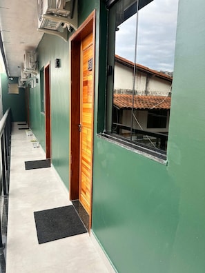 A corridor with green walls, wooden doors, and a window with a view of a building with a tiled roof. - Morada do Sol Suítes (Arraial do Cabo)