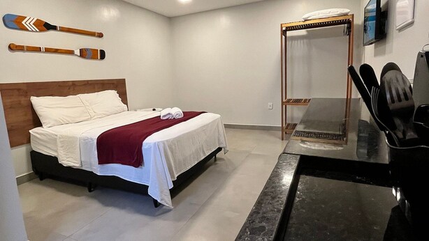 A bedroom with a bed, a bedside table, a mirror, and a wall-mounted television. - Morada do Sol Suítes (Arraial do Cabo)