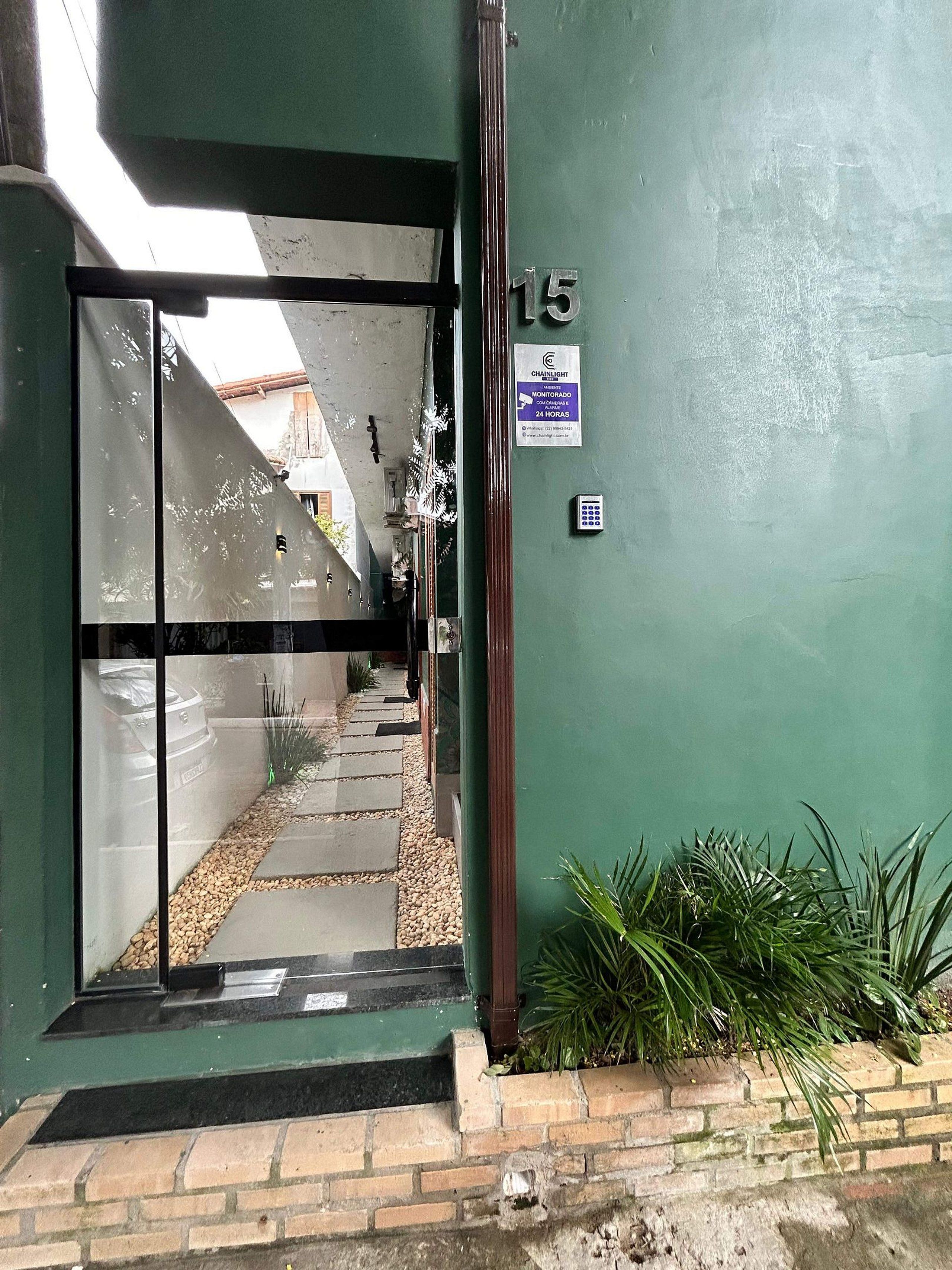 A building entrance with a green wall, a number '15' sign, a security keypad, and a pathway leading to a car.