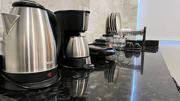 Une cuisine avec un plan de travail noir, une machine à café, une bouilloire et un four à micro-ondes.