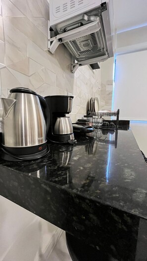 A kitchen with a black countertop, a coffee maker, a kettle, and a microwave. - Morada do Sol Suítes (Arraial do Cabo)