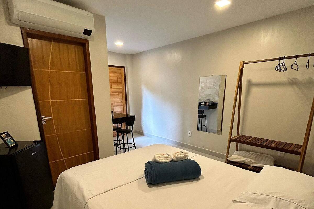 A hotel room with a bed, a desk, a chair, a mirror, and a door.