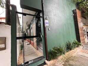 A building entrance with a green wall, a numbered door, and a small garden area. - Morada do Sol Suítes (Arraial do Cabo)