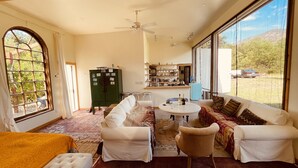 A spacious living room with a large window, a green cabinet, a kitchen area, and a cozy seating arrangement.