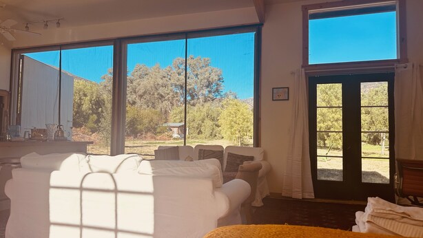 A room with a bed, a sofa, and a large window with a view of trees and a house.