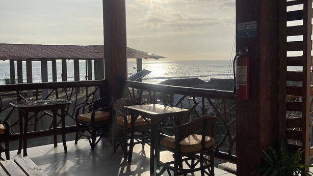 An outdoor patio with wooden tables and chairs, overlooking the sea.