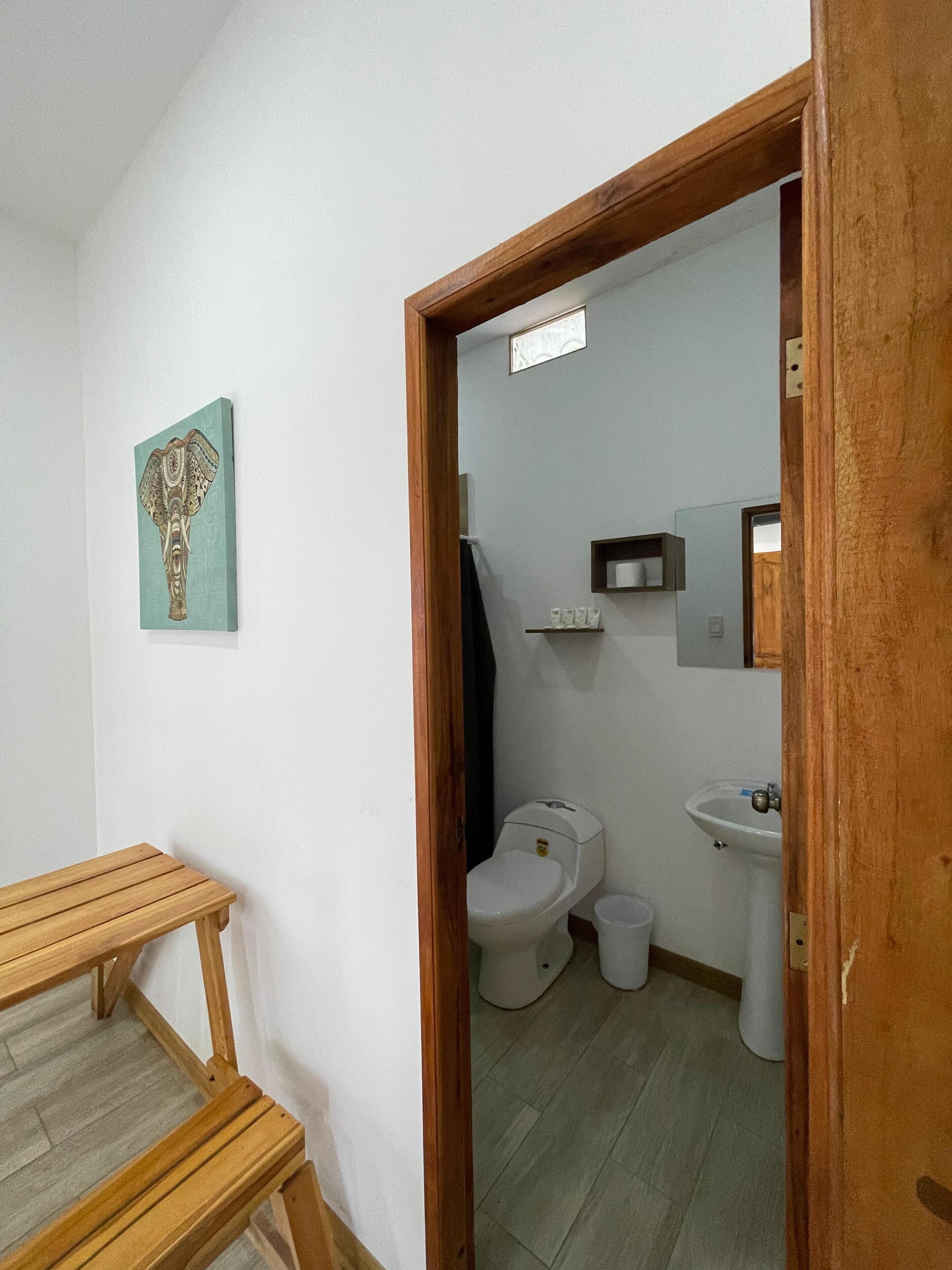 Un baño con inodoro, lavamanos y una banca de madera.
