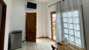 A room with a wooden bench, a small table with a bottle, a wall-mounted TV, and a ceiling fan.