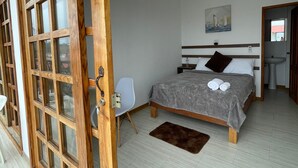 A bedroom with a bed, a chair, a painting, and a bathroom visible through an open door.