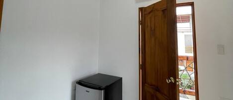 A small room with a refrigerator, a television mounted on the wall, and a wooden door leading to an outdoor area.
