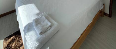 A neatly made bed with white linens and a brown pillow, a bedside table with a phone and a small lamp, and a painting on the wall above the bed.