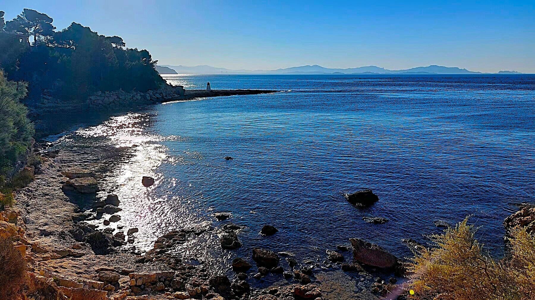 A coastal landscape with rocky terrain and a lighthouse in the distance.