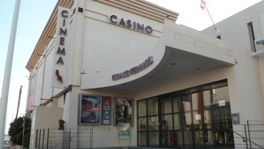 Un bâtiment abritant un cinéma et un casino, avec une entrée incurvée, des affiches sur la façade et une statue devant.