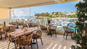 Une terrasse meublée de mobilier en osier, une vue sur un port de plaisance et une grande roue en arrière-plan.