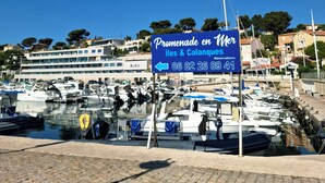 Un port de plaisance avec des bateaux amarrés, une enseigne indiquant « Promenade en mer », et un bâtiment portant l’inscription « BLEU » à l’arrière-plan.