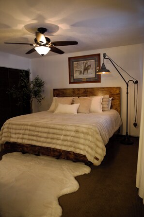 Ein Schlafzimmer mit einem Bett, einem Deckenventilator, einer Stehlampe, einem gerahmten Bild an der Wand und einer Pflanze.